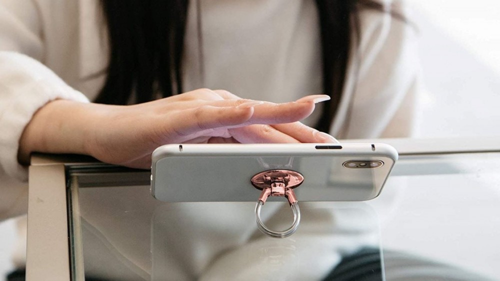 A woman using the Aduro Phone Ring in Rose-Gold as a desktop phone stand.